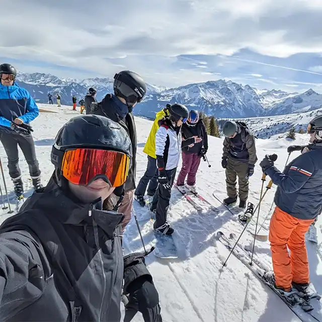 Gruppe von Kolleginnen und Kollegen bei der Snow Academy 2025, auf einer Skipiste, bereit zur Abfahrt – mit beeindruckender Bergkulisse im Hintergrund bei sonnigem Wetter.