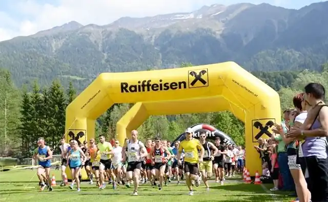 Läuferinnen und Läufer starten bei einem Stadtmarathon unter einem gelben Raiffeisen-Bank-Torbogen.