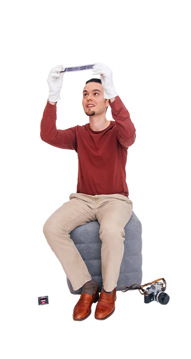 Jan-Bartl Koncel, MSc (WU) sitzt auf einem Hocker und trägt weisse Handschuhe, während er ein Fotonegativ prüfend gegen das Licht hält - mit Liebe zur analogen Fotografie.