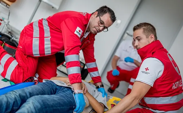 Rettungssanitäter des Österreichischen Roten Kreuzes bei einer Erste-Hilfe-Massnahme. Bild betont den humanitären Einsatz und die medizinische Versorgungskompetenz.
